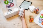 Hand holding a bottle of health supplements with vitamins, gummies, and tablets on a desk, representing business opportunities in Malaysia’s wellness sector.